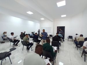 WhatsApp Image 2026-07-06 at 112151 1 - كلية التجارة والعلوم السياسية Bright classroom filled with people seated in chairs, reading and taking notes during a meeting or class.