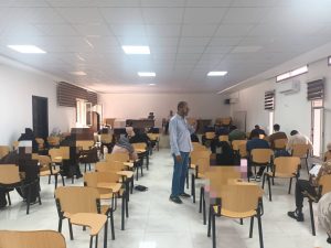 WhatsApp Image 2026-07-06 at 112151 2 - كلية التجارة والعلوم السياسية A classroom full of students seated at desks while a man in a light blue shirt stands at the front teaching.