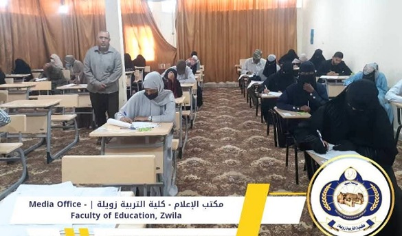 Students taking an exam in a classroom; a supervisor stands at the back. A banner at the front reads 'Media Office - Faculty of Education, Zwila' and a circular logo appears in the bottom right.