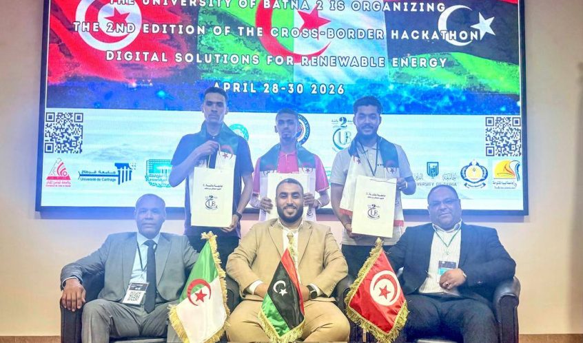 Winners pose with certificates on a stage at the Cross-Border Hackathon 2026 in Batna; three flags (Algeria, Libya, Tunisia) on the table in front of them.