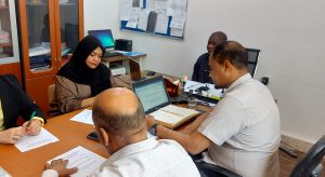 A group of professionals seated around a conference table reviewing documents, with laptops and notebooks open.