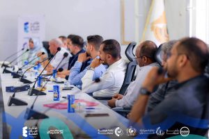 FB_IMG_1781127222650 - كلية الصيدلة - جامعة سبها Panel of diverse professionals seated at a long conference table with microphones during a meeting