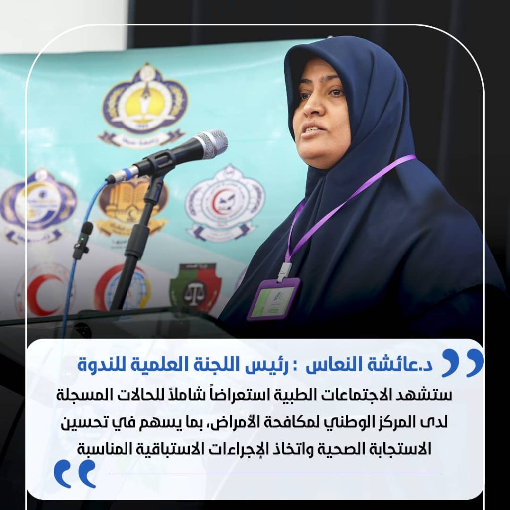 Woman in a navy hijab speaking at a podium with a microphone, wearing a purple ID badge on a lanyard.