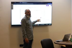 1B2538EE-71CC-4B22-BCA6-860289C185EF - جامعة سبها | Sebha University Man with gray beard presenting a Google Forms screen on a wall monitor in a meeting room of̈fice/education setting