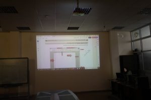 Projected screen displaying a Word document with a flowchart and red arrows in a dim classroom setting.