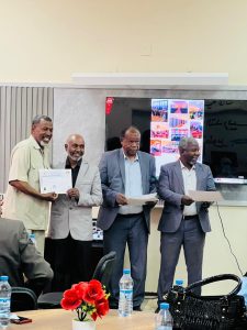 Four men in suits stand at a ceremony; one hands a certificate to another while others hold papers.