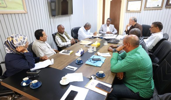 Group of professionals seated around a long conference table, engaged in a meeting with papers and notebooks nearby.