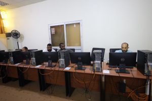 Five men sit at Dell desktop computers in a computer lab, with orange cables running across a long wooden table.