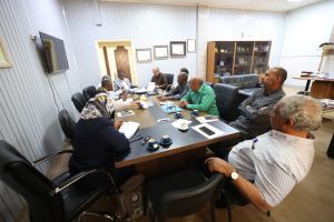 Group of people seated around a conference table in discussion, papers and coffee cups visible on the table in a formal meeting room
