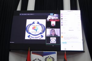 Large conference screen showing a Zoom-style meeting with a central logo reading ‘Cognitive Science Lab 2024,’ participant thumbnails, and a chat panel on the right; flags at the front of the stage.