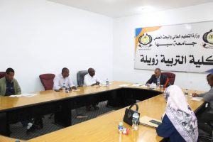People seated around a U-shaped conference table in a bright meeting room, with a large Arabic banner for Sebha University on the wall behind them.