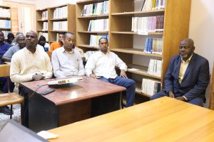 Group of adults seated in a library classroom, listening to a presentation near shelves of books behind them.