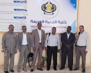 Six men in business attire posing for a group photo in front of a banner that reads 'Faculty of Education' (Al-Ghuraifah).