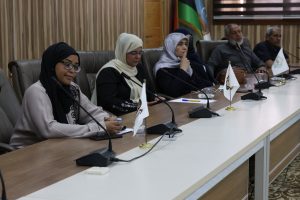 Dive into a conference room: diverse panel wearing hijabs seated at a long table with microphones and small flags in front of them.