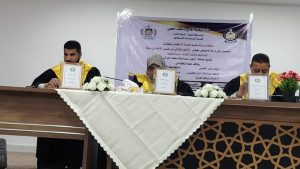 Three academics in yellow robes sit at a conference table displaying framed certificates during a formal award ceremony.