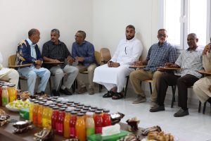 Men sitting in a semicircle in a bright room, having a discussion, with snacks and juice bottles on a table in the foreground.