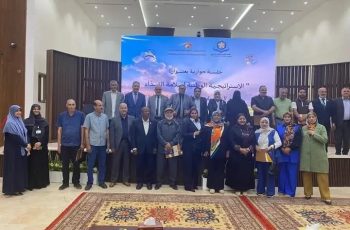 Group of men and women posing for a group photo on a conference stage with a blue banner behind them.