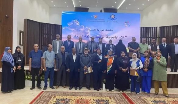 Group of men and women posing for a group photo on a conference stage with a blue banner behind them.
