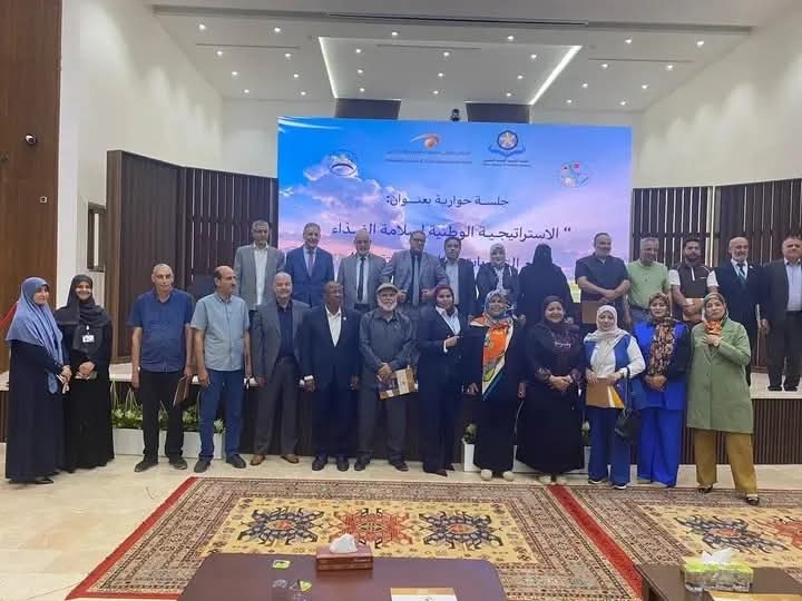 Group of men and women posing for a group photo on a conference stage with a blue banner behind them.