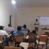 Teacher giving a presentation at the front of a classroom with students seated at desks facing him.
