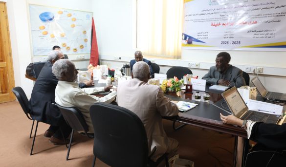 Group of men seated around a conference table in a meeting room, with laptops, paperwork, and gift bags on the table, banner on the wall behind them.