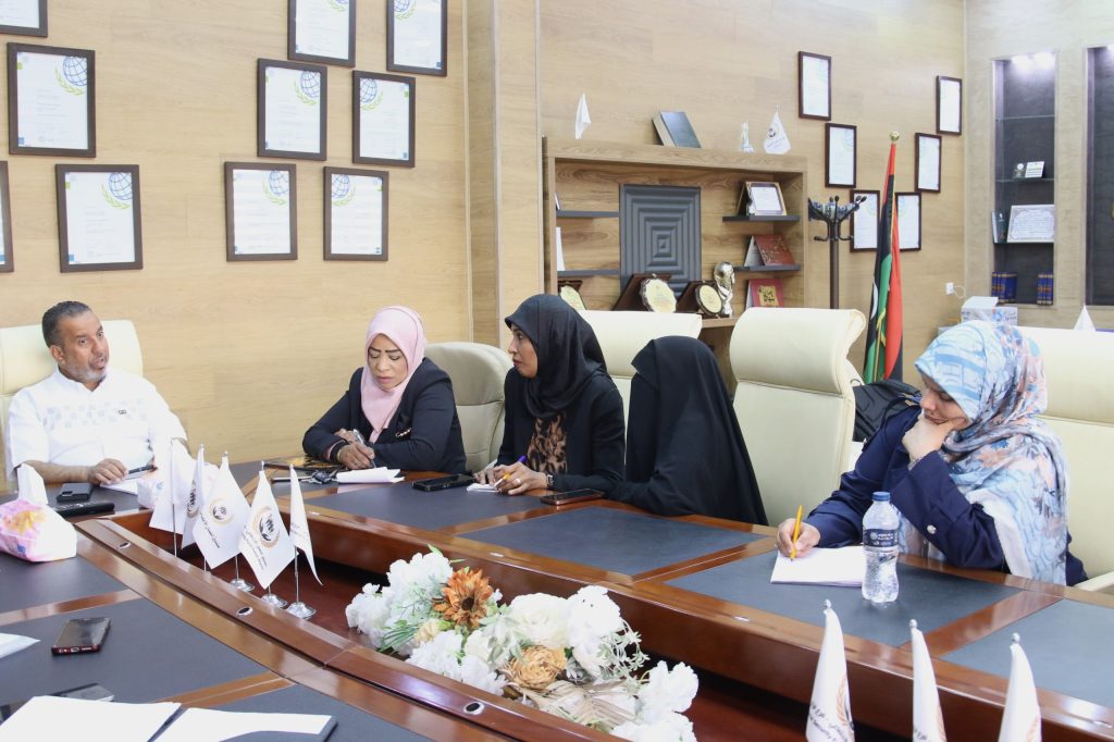 Group of professionals seated around a conference table, discussing in a room with framed certificates and flags on the wall behind them.