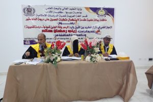 5FDACBC0-CD23-4B35-9DB8-CE1E648A5B87 - جامعة سبها | Sebha University Panel of three academics in robes seated at a table during a conference with a large Arabic banner behind them.