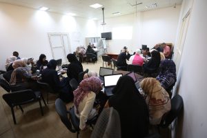 6B54F783-90F8-4F97-9993-38CDC1E8D885 - جامعة سبها | Sebha University Group of people in a classroom, many women wearing hijabs, working on laptops around tables during a workshop.