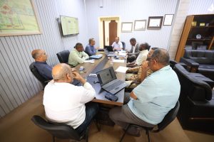 Group of men in a conference room seated around a long table with laptops and papers, engaged in a discussion.