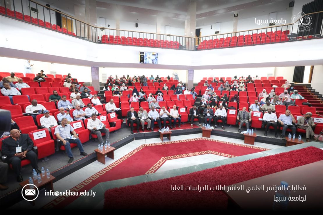 Audience seated in a large auditorium with red chairs during a formal academic conference at Sebha University in Libya.