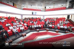 7E64D01E-5683-4A00-8599-DD6E3832DB16 - جامعة سبها | Sebha University Audience seated in a large auditorium with red chairs during a formal academic conference at Sebha University in Libya.