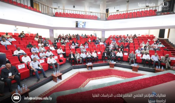 7E64D01E-5683-4A00-8599-DD6E3832DB16 - جامعة سبها | Sebha University Audience seated in a large auditorium with red chairs during a formal academic conference at Sebha University in Libya.