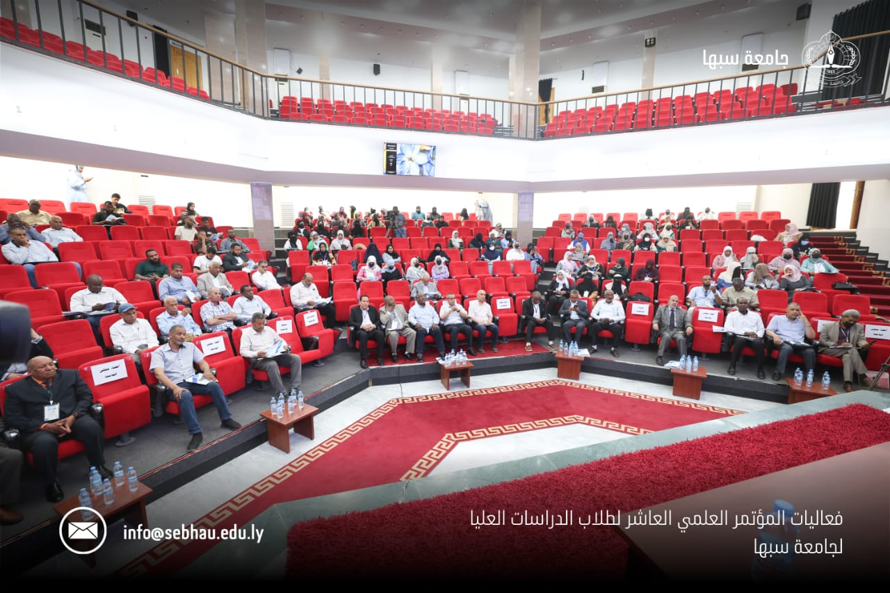 Audience seated in a large auditorium with red chairs during a formal academic conference at Sebha University in Libya.