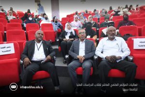 B25FC5BD-563E-48EA-8F01-C8C18168E786 - جامعة سبها | Sebha University Group of diverse attendees in a red-velvet lecture hall, front-row focused, at a Sebha University event with logos and Arabic caption visible.
