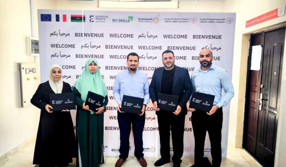 B6DEA6D4-B9CA-44CA-832C-2AC280B3971C - جامعة سبها | Sebha University Five people pose together indoors in front of a 'Bienvenue Welcome' backdrop, each holding dark folders.