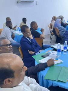 CAAE55F2-3543-4C2A-9729-A07A8822C1C6 - جامعة سبها | Sebha University People seated around tables at a meeting or conference, with notebooks and water bottles visible in a bright room.