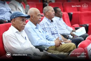 CC3ADA52-E4A2-4F1C-B424-24A4BE1D77F4 - جامعة سبها | Sebha University Senior men seated in red theater seats at a university conference, with Sebha University logo in the top right and the email info@sebhau.edu.ly at the bottom left.