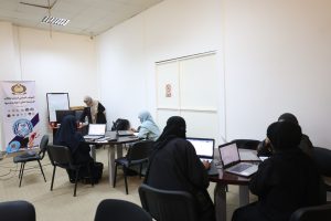 CCCC0434-8179-41CB-83ED-4FA89904B590 - جامعة سبها | Sebha University Women in hijabs seated around laptops at a classroom-style meeting with a vertical banner on the left.