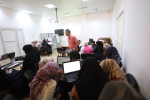 D077EB30-8579-46C2-B17D-B5534AFB55CF - جامعة سبها | Sebha University Instructor standing with a laptop in a classroom full of students using laptops for a training session.