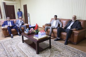 D48D89A5-29AD-41DA-B629-033336ADDA7E - جامعة سبها | Sebha University Four men in suits sitting on brown leather couches in a conference room, with a coffee table full of drinks in front of them.