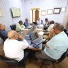 Group of professionals seated around a conference table in an office, with laptops, papers, and coffee cups