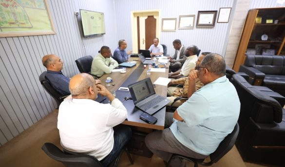 Group of professionals seated around a conference table in an office, with laptops, papers, and coffee cups