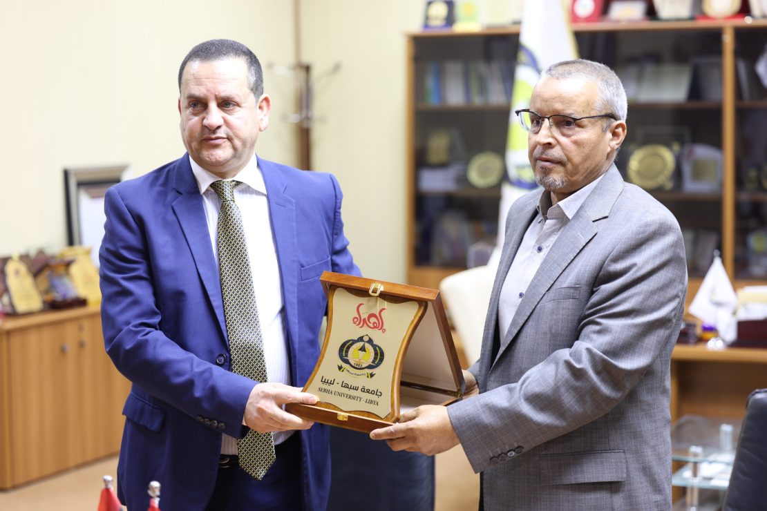 Two men in suits exchange a framed wooden plaque during an award ceremony in an office.