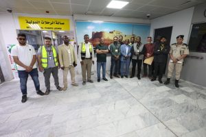 Group of men posing for a photo inside an airport terminal under a yellow 'International Flights Lounge' sign