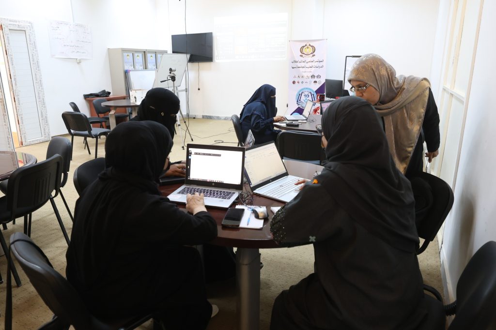 F3CF792B-62B4-4AD7-A8EF-F0BBBED17384 - جامعة سبها | Sebha University Women in hijabs seated around a table with laptops in a classroom or conference room, collaborating on a project.