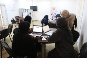 F3CF792B-62B4-4AD7-A8EF-F0BBBED17384 - جامعة سبها | Sebha University Women in hijabs seated around a table with laptops in a classroom or conference room, collaborating on a project.