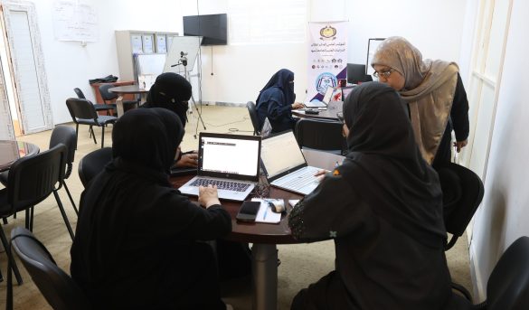 F3CF792B-62B4-4AD7-A8EF-F0BBBED17384 - جامعة سبها | Sebha University Women in hijabs seated around a table with laptops in a classroom or conference room, collaborating on a project.