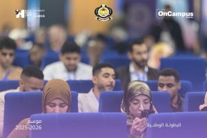Audience seated in blue theater chairs at a conference, two women in hijabs in the foreground, event logos across the top, Arabic captions for season 2025–2026 and the national championship visible in the image.