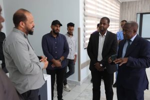 Group of men in business-casual and formal attire stand in a modern office lobby, chatting.