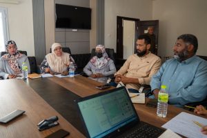 WhatsApp Image 2026-05-14 at 12.06.33 PM (1) - جامعة سبها | Sebha University Six people seated around a wooden conference table in a meeting room, with notebooks, pens, and water bottles visible as they discuss.